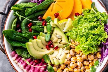 Healthy salad vegan, detox dish with roasted chickpeas, avocado, persimmon, spinach, avocado, watermelon radish and seeds. Top view, flat lay