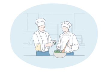 Cooking, professional chef, restaurant concept. Young man and woman professional cooks in aprons and hats cooking healthy salad or dish together in kitchen of cafe Gourmet, delicious, tasty menu 