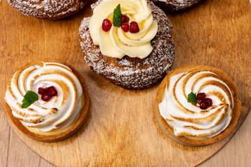 sweet dessert eclair shu with custard with pomegranate syrup and tartlet with white whipped cream on a wooden table. cafe concept