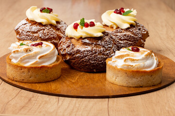 sweet dessert eclair shu with custard with pomegranate syrup and tartlet with white whipped cream on a wooden table. cafe concept