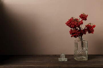 Fototapeta na wymiar Old fashioned glass decanter and ripe viburnum bunch on the wooden deskagainst brown background.Empty space