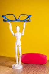 wooden mannequin holding blue glasses in a yellow background