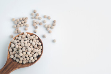 White pepper in a wooden spoon on a white background.