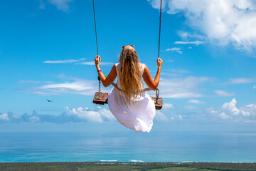 Woman swinging on swings over the green mountains with ocean sea caribbean tropical landscape and...