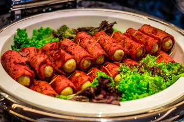 A buffet offering of chicken hot dogs wrapped in ham and skwered with a toothpick