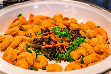 A buffet offering of deep fried breaded shrimp served in a white serving tray