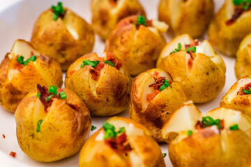 a buffet offering of baked baby potatoes served with bacon bits and spring onions on top