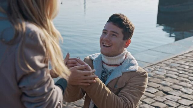 Handsome young man in love standing on one knee and holding a ring while proposing to girlfriend on pier. Love, family, relationship, wedding concept. Filmed on REd 4k, 10 bit color