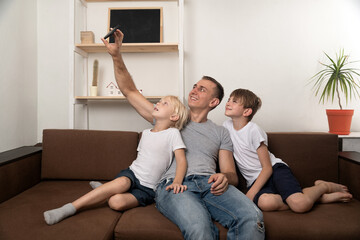 Fototapeta na wymiar Father and two sons take a selfie while sitting on the couch. Leisure with children
