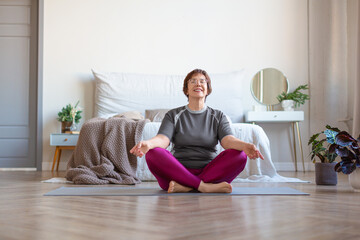An elderly woman meditates at home in the lotus position. The concept of a healthy lifestyle.