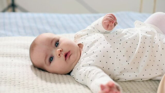 Little clever baby girl resting on bed with mom looking at camera with thoughtful eyes smiling enjoying beautiful day. Family lifestyle. Health care concept. Female child innocence. Sunny background.
