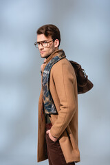 stylish man in winter coat and glasses standing with hand in pocket holding leather briefcase on grey