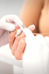 Close up of a manicurist files the female nails with the nail file in a nail salon