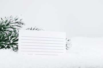 White sheet in a ruler, in the snow, near a Christmas tree branch. Christmas and New Years concept. Copy space