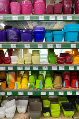Variety of colorful flower pots are sold at the store. Rows of different pots for indoor plants on shelves in a mall. Vertical view.