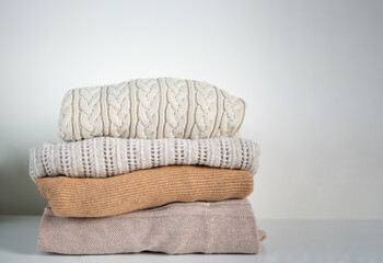 Housework, Stack of cozy knitted sweaters beige tone on a white table. Retro style. Warm concept