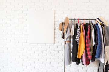 Rack with colorful clothes on hangers and frame canvas for mock up over white brick wall background