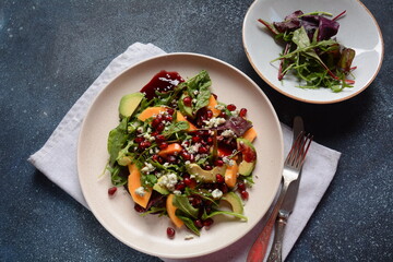 Healthy salad persimmon, blue cheese, spinach, arugula, lettuce leaves on white plate