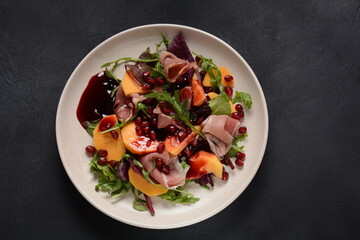 Salad with slices of bacon, persimmon, spinach, arugula, lettuce leaves  and pomegranate seeds and honey sauce