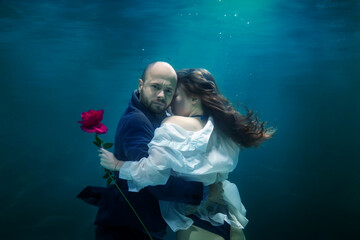 Young businessman embraces his woman, gives rose, kisses beloved, underwater. Emotional happy couple in pond. Concept romantic date, surprise and commitment to development of relations. Copy space