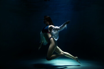Slender pretty young woman brunette in bathing suit and white blouse in dark pond, illuminated by moonlight. Elegant female underwater. Concept of beauty, tenderness and striving for ideal. Copy space