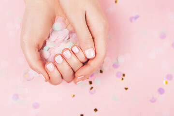 Obraz na płótnie Canvas Manicure and nail care concept. Woman hands are holding pastel confetti. Perfect pastel pink nail polish. Party, holidays or celebration vibes.