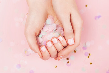 Manicure and nail care concept. Woman hands are holding pastel confetti. Perfect pastel pink nail polish. Party, holidays or celebration vibes.