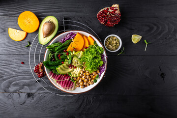 Healthy vegetarian food concept. vegan, detox Buddha bowl dish with roasted chickpeas, avocado, persimmon, spinach, avocado, watermelon radish and seeds