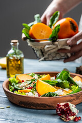 Persimmon salad with spinach, nuts, goat cheese, pomegranate, pumpkin seeds. food prepare in process vegetarian salad by chef hand in home kitchen. Healthy vegetarian food concept