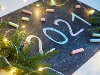 New year 2021 written in colored chalk on a blackboard dark for chalk. Spruce branches. Garland lights.