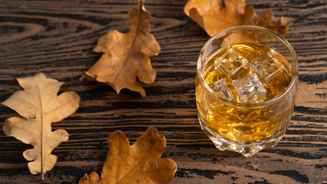Conceptual image on the subject of alcoholism. Whiskey in a glass and autumn leaves on a wooden table