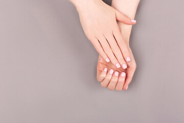 Manicure and nail care concept. Minimal composition of the woman hands on the grey background. Classic pink nail polish. Flat lay, top view.