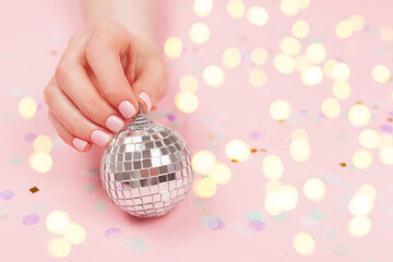 Christmas and New Year background. Woman hands are holding a Christmas ball. Perfect pastel pink nail polish. Party, festive, holidays or  celebration vibes.