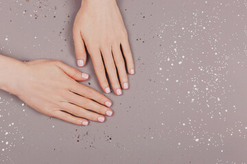 Christmas and New Year background. Woman hands and glitter. Perfect pastel pink nail polish. Party, festive, holidays or celebration vibes. Minimal composition.