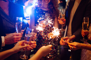 Glowing sparkles in hands. Group of happy people enjoying party with fireworks. Winter holiday,...