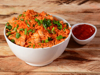 Tasty schezwan chicken fried rice with tomato sauce served in white bowl over a rustic wooden...