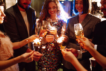 Glowing sparkles in hands. Group of happy people enjoying party with fireworks. Winter holiday, youth, lifestyle concept.
