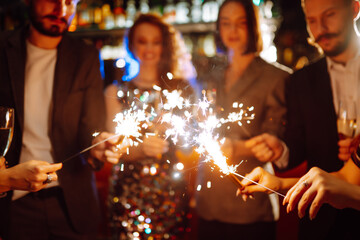 Glowing sparkles in hands. Group of happy people enjoying party with fireworks. Winter holiday, youth, lifestyle concept.
