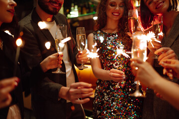 Glowing sparkles in hands. Group of happy people enjoying party with fireworks. Winter holiday, youth, lifestyle concept.