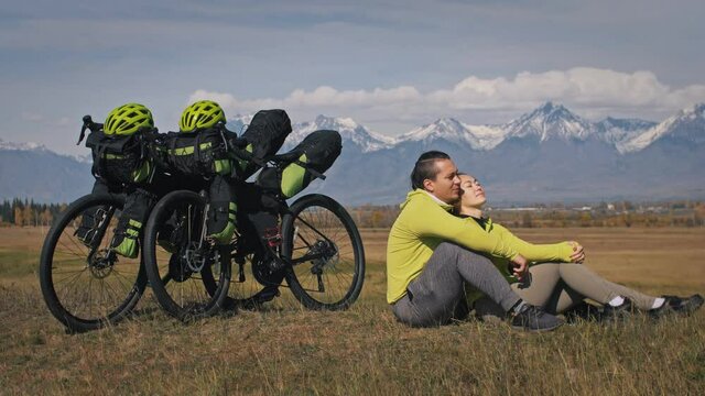 The man and woman travel on mixed terrain cycle touring with bikepacking. The two people journey with bicycle bags. Sport bikepacking, bike, sportswear in green black colors. Mountain snow capped.