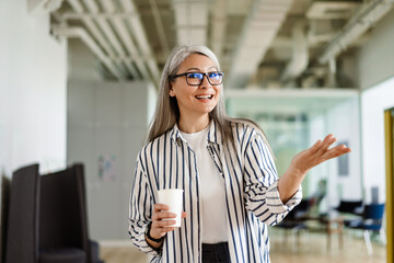 Happy white-haired mature woman holding copyspace while drinking coffee