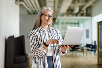 Happy white-haired mature woman smiling while using laptop