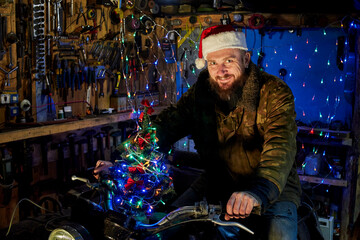 Fototapeta na wymiar A man in a santa claus hat sitting on a motorcycle in the garage on New Year's Eve.