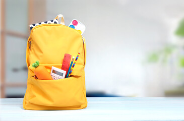 Yellow backpack with school supplies on wooden table empty copy space background.Knapsack with tools and accessories indoors.