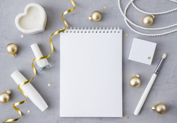 Winter template with blank Notepad with women's accessories, cosmetics, candle and Christmas tree balls on a gray concrete background. The concept of a diary, holiday greeting or planning.