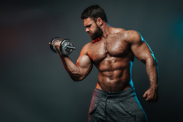 Obraz na płótnie Canvas Muscled shirtless man with dumbbell doing his biceps exercise. Male body in colourful lightning in studio. Big hunk with six pack abs exercises in studio at grey background.