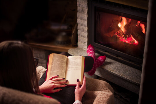 Female reading a book by the fireplace