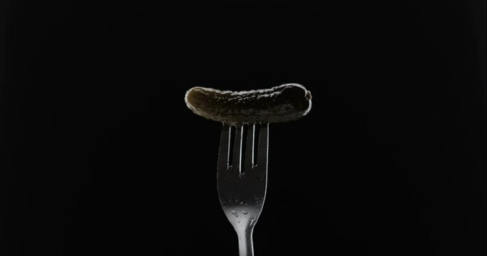 Rotating fork with gherkin on black background
