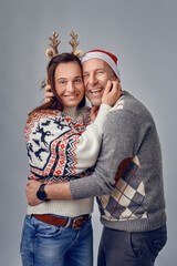 Middle-aged happy couple laughing and hugging each other wearing a santa hat and an elk headband