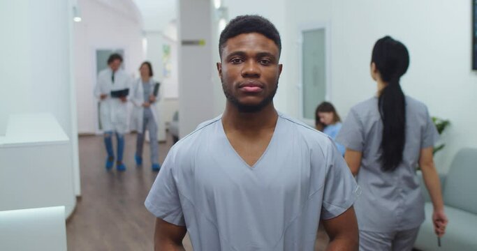 African American young male healthcare worker standing in clinic hall and looking at camera in good mood. Handsome man physician at work in hospital. Medical concept. Close up portrait